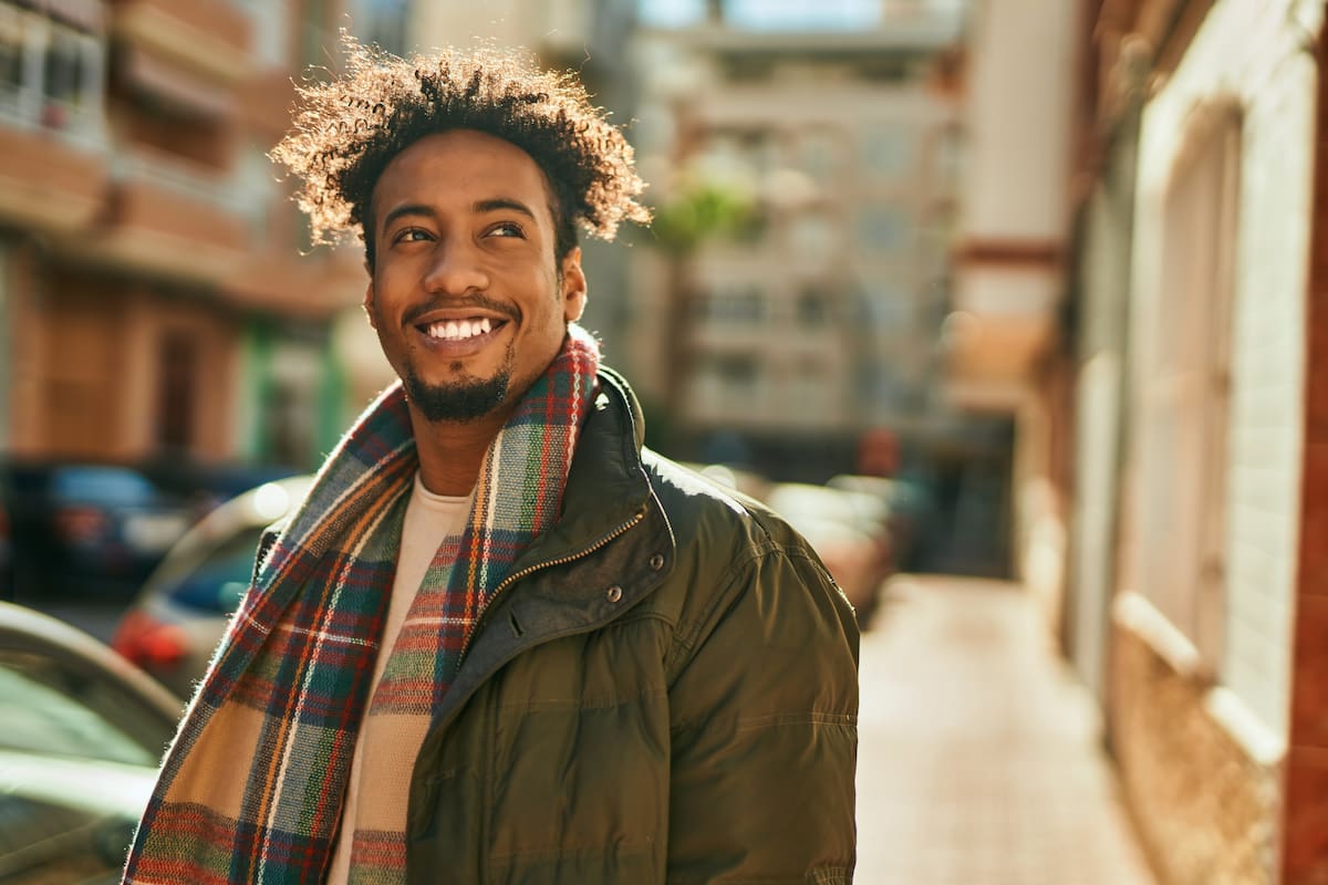 Man wearing coat and scarf smiling and walking down street