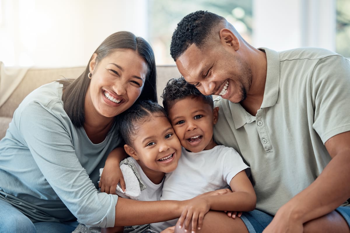 A family of four smiling and sitting together on a couch