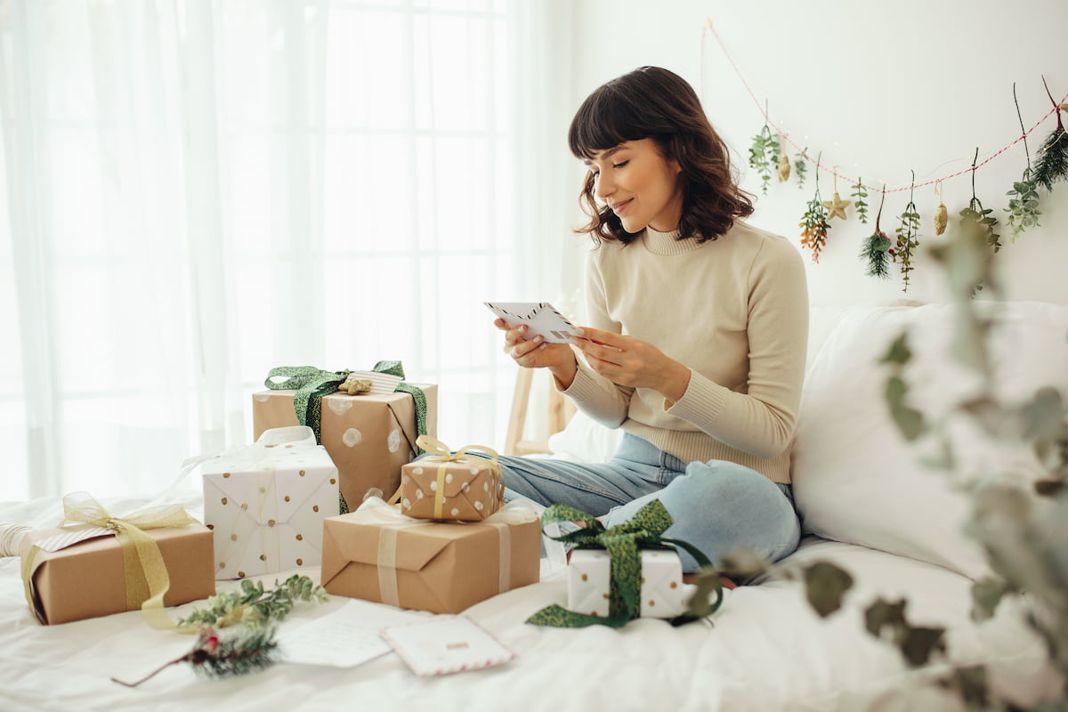 A woman sitting and opening presents on her bed