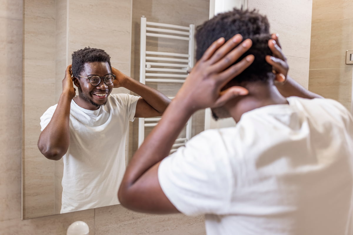 A man with glasses looking at his hair in a mirror.